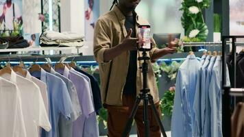 Content creator filming in clothing store with elegant assortment of clothes. Influencer contracted to advertise new collection of stylish high class attire garments in premium fashion boutique video