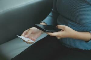 un crédito tarjeta en el manos de un joven mujer de negocios paga para un negocio en un móvil teléfono y en un escritorio con un ordenador portátil. foto