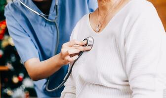 Lady coming to clinic for heart and lungs checkup, male doctor using stethoscope, listening to female patient's breath or heartbeat, sitting in clinic office photo