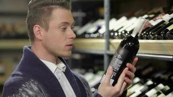 Handsome young man holding bottle of wine while standing in a wine store video