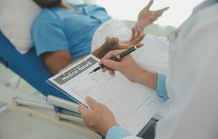 Close up of doctor sitting on bedside of male patient in hospital photo