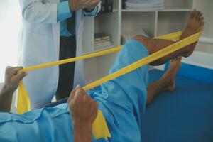 Male patient using elastic band while doing physical exercises for leg muscles at modern clinic, rehabilitation center or hospital. Close up of man's foot. Physiotherapy concept photo