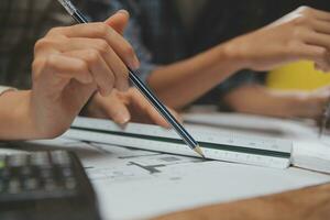 Team of multiethnic architects working on construction plans in meeting room. Engineers discussing on project in office. Mature businessman and woman standing around table working on blueprint. photo