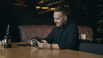 une homme est assis dans une élégant café et les usages une téléphone intelligent. constant la communication est possible Merci à le l'Internet. video