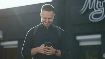 modern städtisch Mann Verwendet ein Smartphone auf ein Stadt Straße. Internet Technologien machen es Einfacher zu Zugriff verschiedene Dienstleistungen und Assistenten mit Handy, Mobiltelefon Anwendungen. video