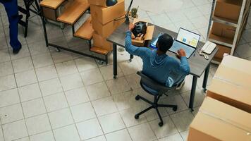 Male startup owner working on financial planning and logistics with laptop, checking merchandise before shipping it. Employee taking notes for stock inventory and sending order. Tripod shot. photo