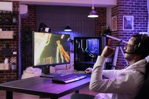 African american gamer ecstatic after killing opponent in online multiplayer shooting game. Man at computer desk having burst of happiness after defeating enemies and winning level photo