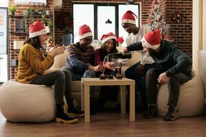 Excited company employees in santa hats gathered in festive decorated office celebrating christmas together. Happy cheerful coworkers enjoying new year dinner at corporate party photo