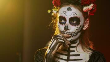 Scary young adult thinking about santa muerte in studio, acting thoughtful and pensive on day of the dead mexican holiday. Woman portraying holy cavalera catrina halloween goddess. Handheld shot. photo