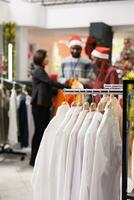 Selective focus of staff helps client in clothing store, presenting new clothing line models to buy on sale. Retail employees assisting customer to choose festive dinner outfit for christmas eve. photo