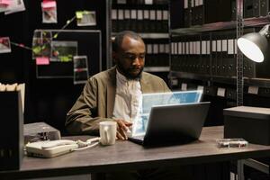 Young investigator analyzing augmented reality clues, examining evidence and case files in private incident room. Private detective trying to solve felony with artificial intelligence hologram. photo