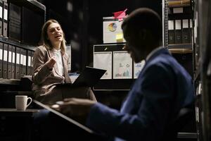 Police officers analyzing confidential federal files, working overhours at mysterious criminal case in arhive room. Criminology team checking crime scene evidence, discovering victim report photo