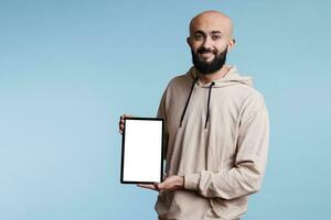 Smiling arab man presenting advertisement on digital tablet white blank screen portrait. Cheerful person holding portable gadget and showing mock up for software application promotion photo