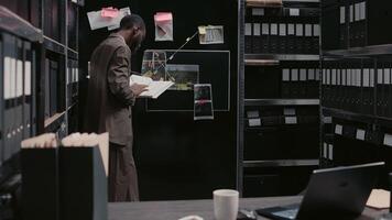 Young policeman examining detective map with evidence, trying to solve crime or felony. Male inspector doing detective work and background checks, using case files for research. Handheld shot. photo