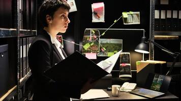 Crime expert reads classified case file to uncover new crime details, evaluating evidence authenticity report in police agency office. Inspector working on private investigation, detective work. photo