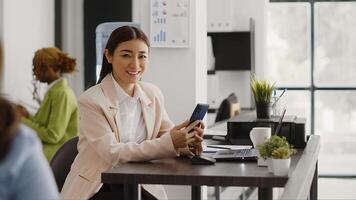 Asian office worker using smartphone app in workplace, planning online report before taking break at desk. Young employee browsing internet and social media app in coworking space. photo