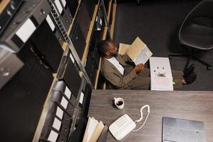 Detective sitting on office floor searching csi report in folder at night time. Exhausted investigator studying crime case files while working on investigation overtime top view photo