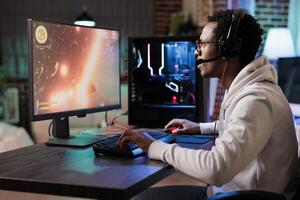 Gamer playing classic arcade spaceship racing videogame, doing flying maneuvres through asteroid clusters. African american man using high tech gaming computer to compete against opponents photo