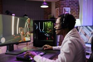 Man in brick wall living room playing immersive video games on gaming PC at computer desk, unwinding after work. Gamer competing against enemies in internet multiplayer shooter photo