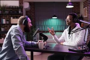 Podcast show host and guest arguing with each other and presenting arguments during online live broadcast in home studio. Men in neon lights decorated living room talking for internet audiences photo