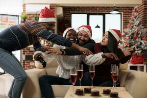 Cheerful coworkers fighting for game console joystick while celebrating christmas in decorated office. Happy diverse colleagues having video gaming competition at new year corporate party photo