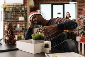 Sad depressed african american man experiencing job failure dismissed from work during holiday season. Unhappy worker packing office belongings after getting fired on xmas eve photo