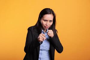 Woman fighter clenching fists to punch in front of camera, preparing for boxing fight in studio. Strong filipino model having angry expression doing fighting gesture, shoowing defense strategy photo