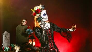 Young scary woman talking on smartphone call, wearing halloween make up and flowers crown in studio. La cavalera catrina using smartphone to chat on dios de los muertos mexican holiday. photo