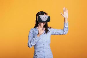 Cheerful woman wearing vr goggles enjoying 3d simultation in studio over yellow background, enjoying digital entertainment. Electronic futuristic experience with augmented tech innovation photo