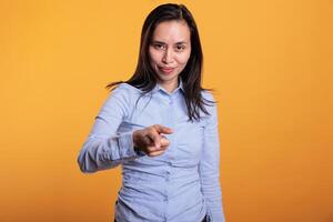 Successful asian woman pointing index finger at you, posing in studio over yellow background. Carefree smiling young adult pointing forefinger advertising promotional product. Advertisement concept photo