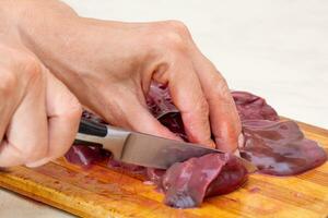 Woman hand cutting beef liver on cutting board photo