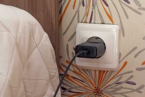 Wall socket with charger plug inside close to bed photo