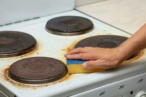 Woman hand remaining burnt stains on dirty electric stove scrubbing using sponge photo