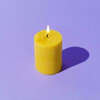 Creative layout of beeswax candle made with natural wax produced by honey bees on pastel violet background. Minimal concept. Trendy beeswax candle composition. photo