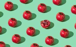 Trendy fruit pattern made of fresh red pomegranates on light pastel green background. Minimal healthy food layout. Nature fruit concept. Pomegranate aesthetic background pattern. photo