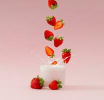 Creative layout made of strawberries falling into glass cup of milk drink with strawberry taste on pastel pink background. Minimal smoothie or milkshake concept. Healthy food for breakfast and snack. photo