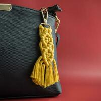 Close-up view of the handmade Macrame key chain hanging on the black hand bag isolated on the red background. photo