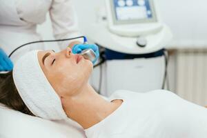 Cosmetology clinic. Professional female cosmetologist doing hydrafacial procedure while being a work. Attractive nice woman lying on the medical bed while having beauty procedures photo