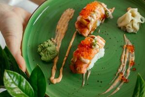 Eating sushi rolls. Japanese food restaurant, salmon maki, gunkan on green plate. Closeup of hand holding plate nigiri rolls. Ginger, wasabi dish photo