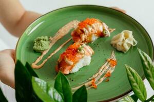 Eating sushi rolls. Japanese food restaurant, salmon maki, gunkan on green plate. Closeup of hand holding plate nigiri rolls. Ginger, wasabi dish photo