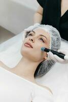Shot of a beautiful young woman on a facial dermapen treatment at the beauty salon. Dermatologist in medical gloves doing hydro peeling procedure. Close up facial treatment. photo
