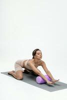 joven mujer haciendo extensión ejercicios en un blanco antecedentes. espuma rodillo masaje pelota, aptitud equipo para desencadenar puntos yo foto