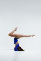 A beautiful slender gymnast in a tracksuit is doing leg split, stretching, yoga in a white studio. photo