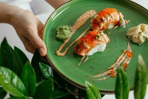 Eating sushi rolls. Japanese food restaurant, salmon maki, gunkan on green plate. Closeup of hand holding plate nigiri rolls. Ginger, wasabi dish photo