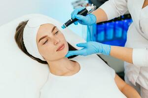 Cosmetology clinic. Professional female cosmetologist doing hydrafacial procedure while being a work. Attractive nice woman lying on the medical bed while having beauty procedures photo