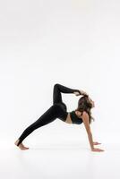 un hermosa esbelto gimnasta en un tramo en un chandal lo hace Deportes o yoga en el estudio extensión foto