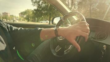 un méconnaissable homme est conduite une auto. dans le tir, mains sont sur le pilotage roue de une prime voiture, le été Soleil inondations le salon et intérieur. video