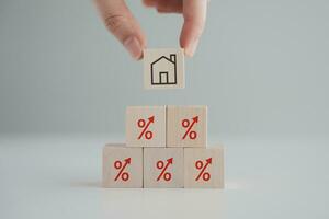 Hand holding house icon on wooden block from red percentage sign with arrow up. Refinance, Interest rates increase, Home loan, Mortgage, House tax. Property investment and asset management concept. photo