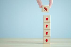 Interest rate finance and mortgage rates. Hand holding percentage sign from rise of arrow up on wooden stack. financial growth, interest rate increase, inflation, sale price and tax rise concept. photo