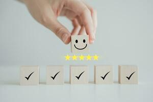 Hand holding smile happy face with 5 star and check mark on wooden block. Feedback rating and positive service review, Customer experience, World mental health day, Emotion, Satisfaction survey. photo